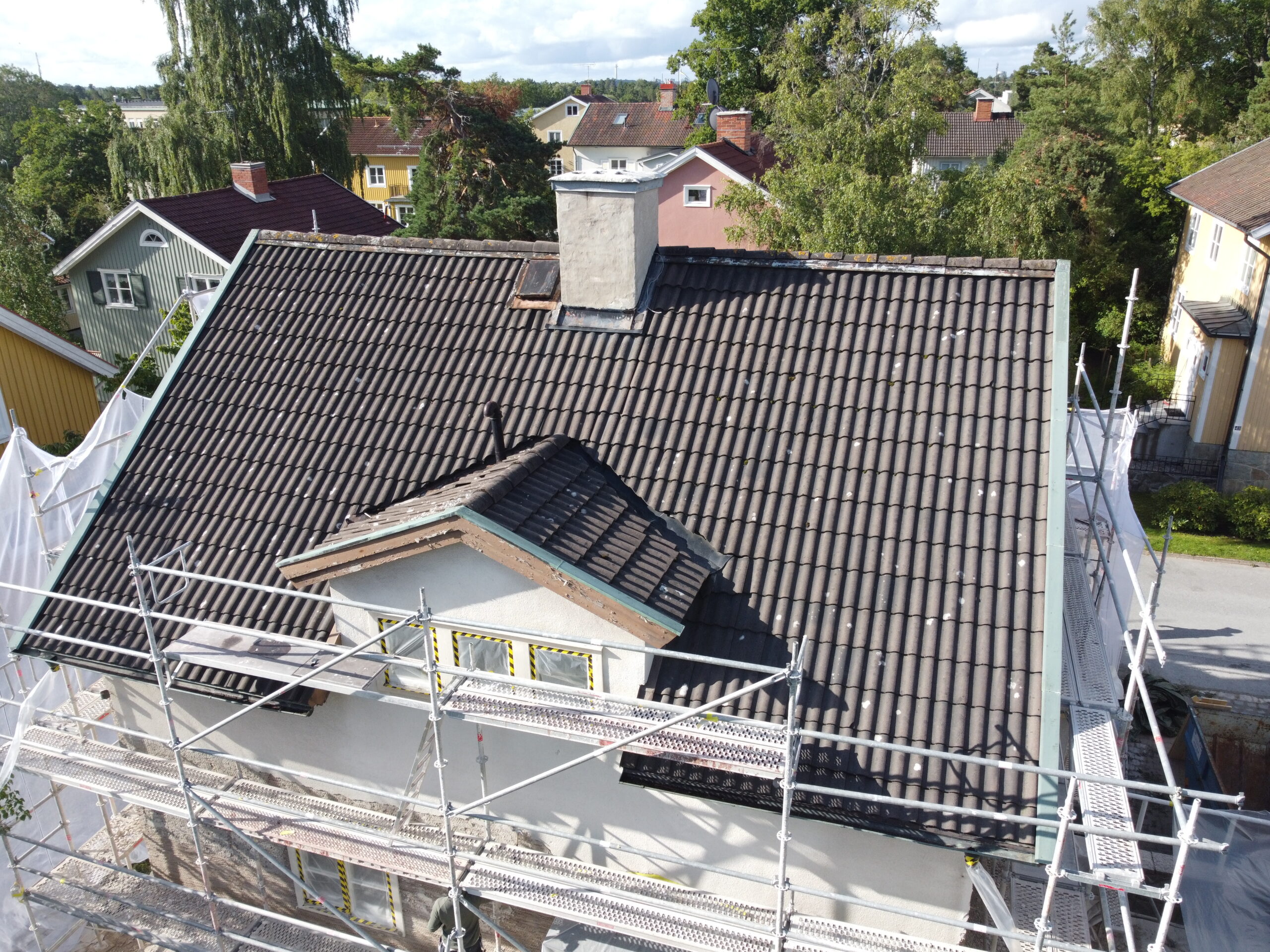 Takomläggning på ett hus med svarta betongpannor. Runt huset står en byggställning.