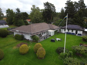 Fågelvy över ett hus med en byggställning runt sig. Bredvid står ett mindre hus med solceller på taket.