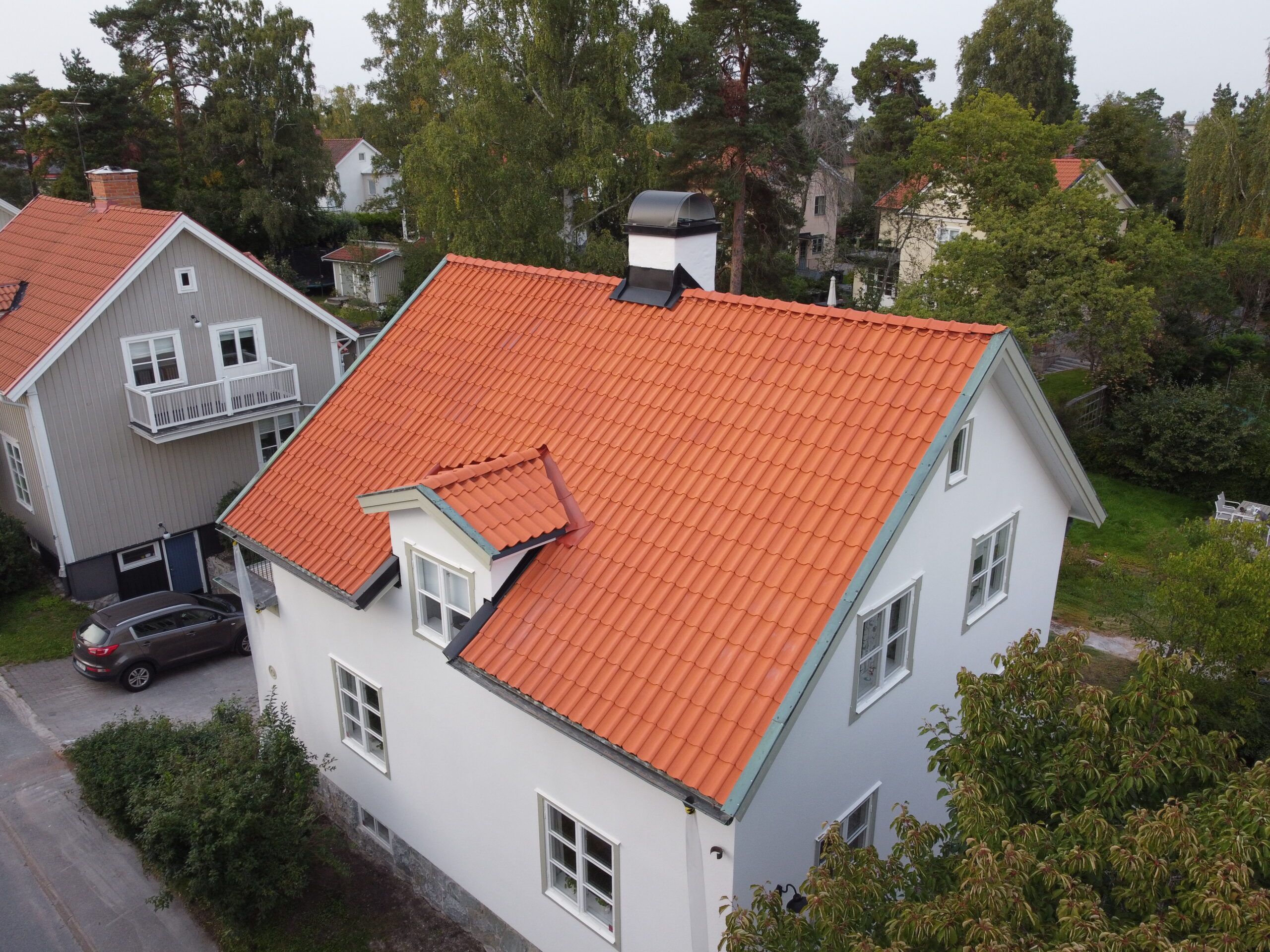 Fågelvy över ett vitt hus med sluttande tak av tegelpannor.