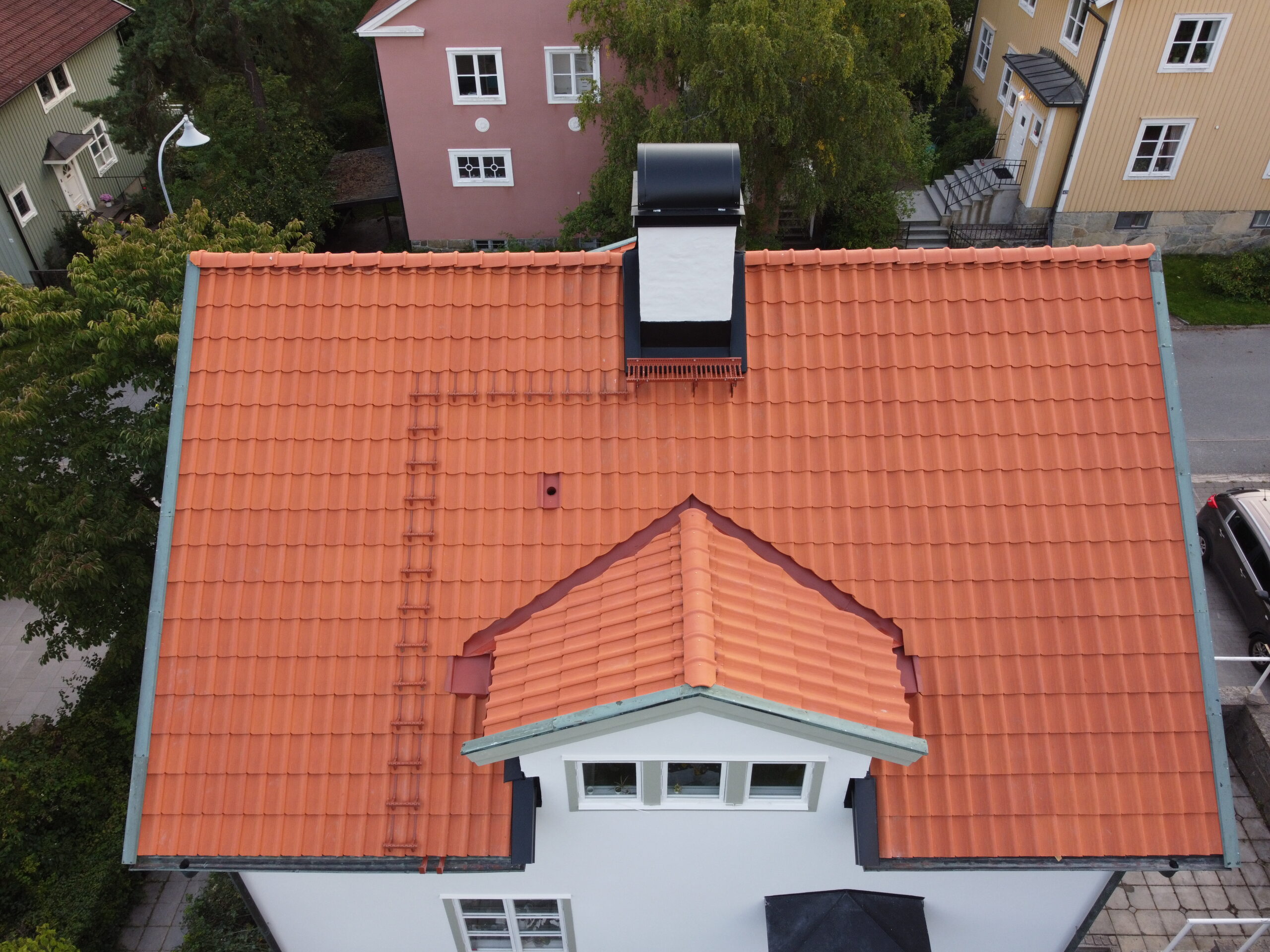 Fågelvy över ett vitt hus med sluttande tak av tegelpannor.