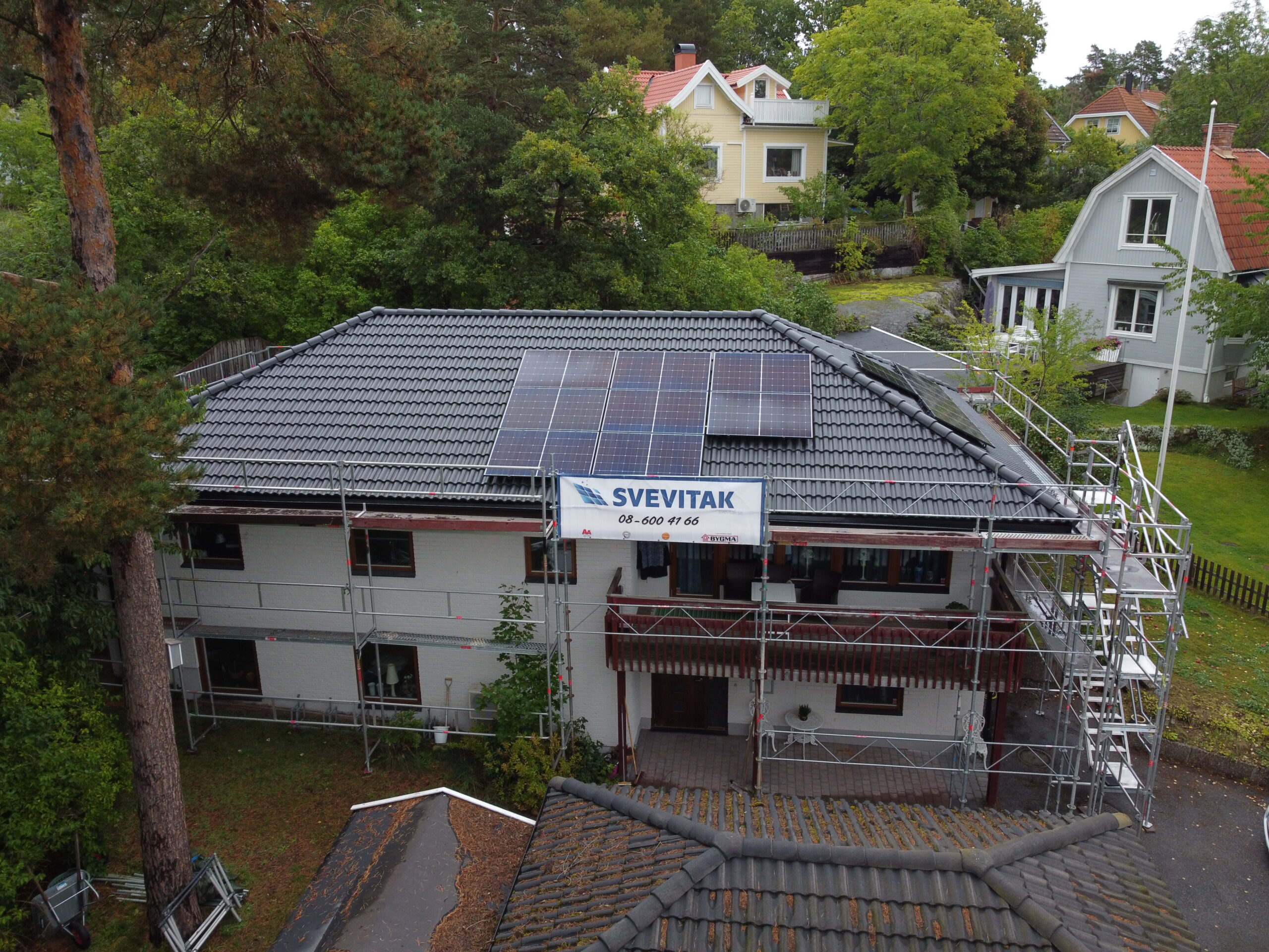 Fågelvy över omlagt tak med betongpannor och solceller. Framför huset står en byggställning med Svevitaks logga