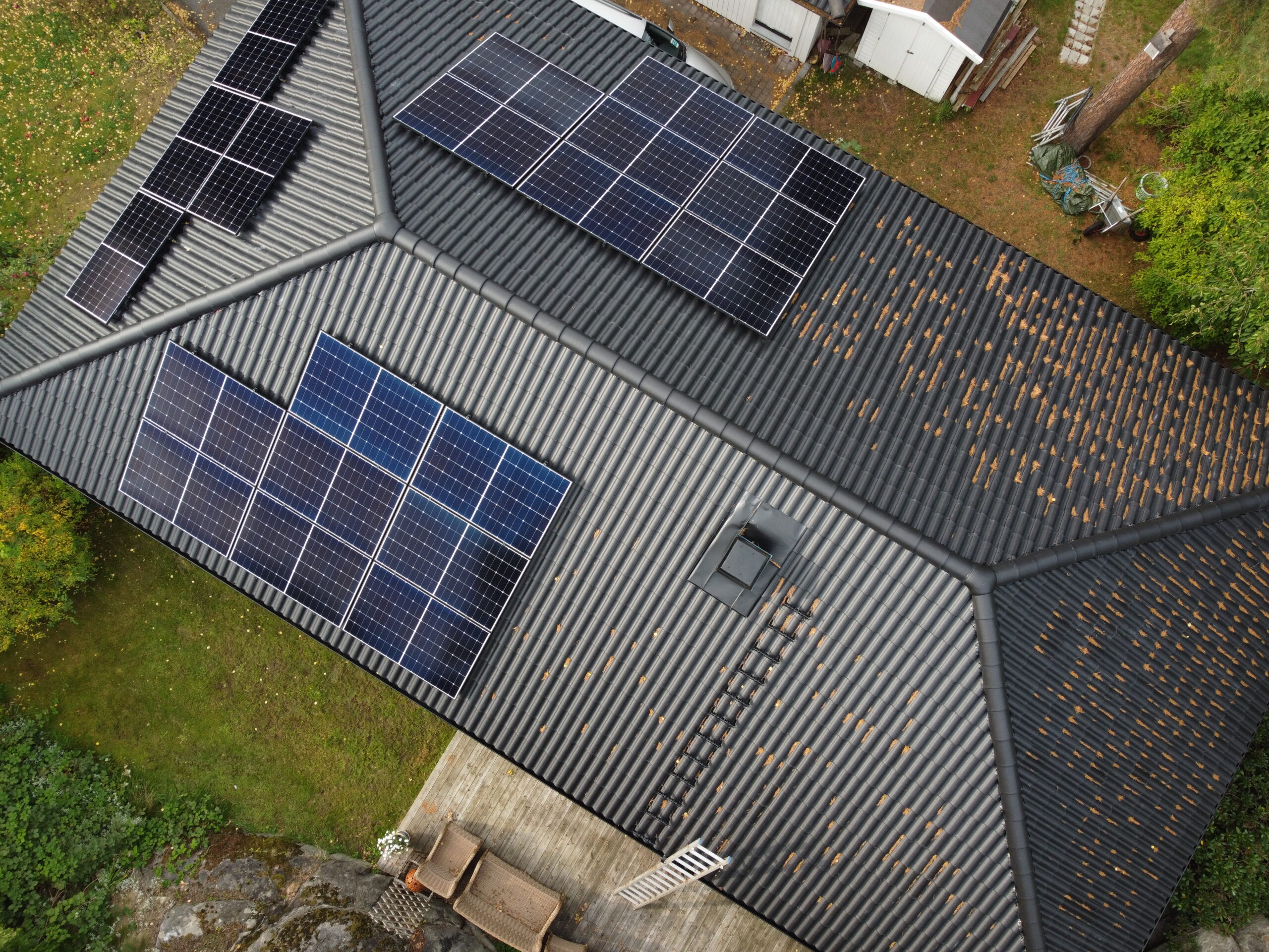 Fågelvy ovanför ett svart hustak med 3 paneler av solceller. Runt huset står en byggställning.