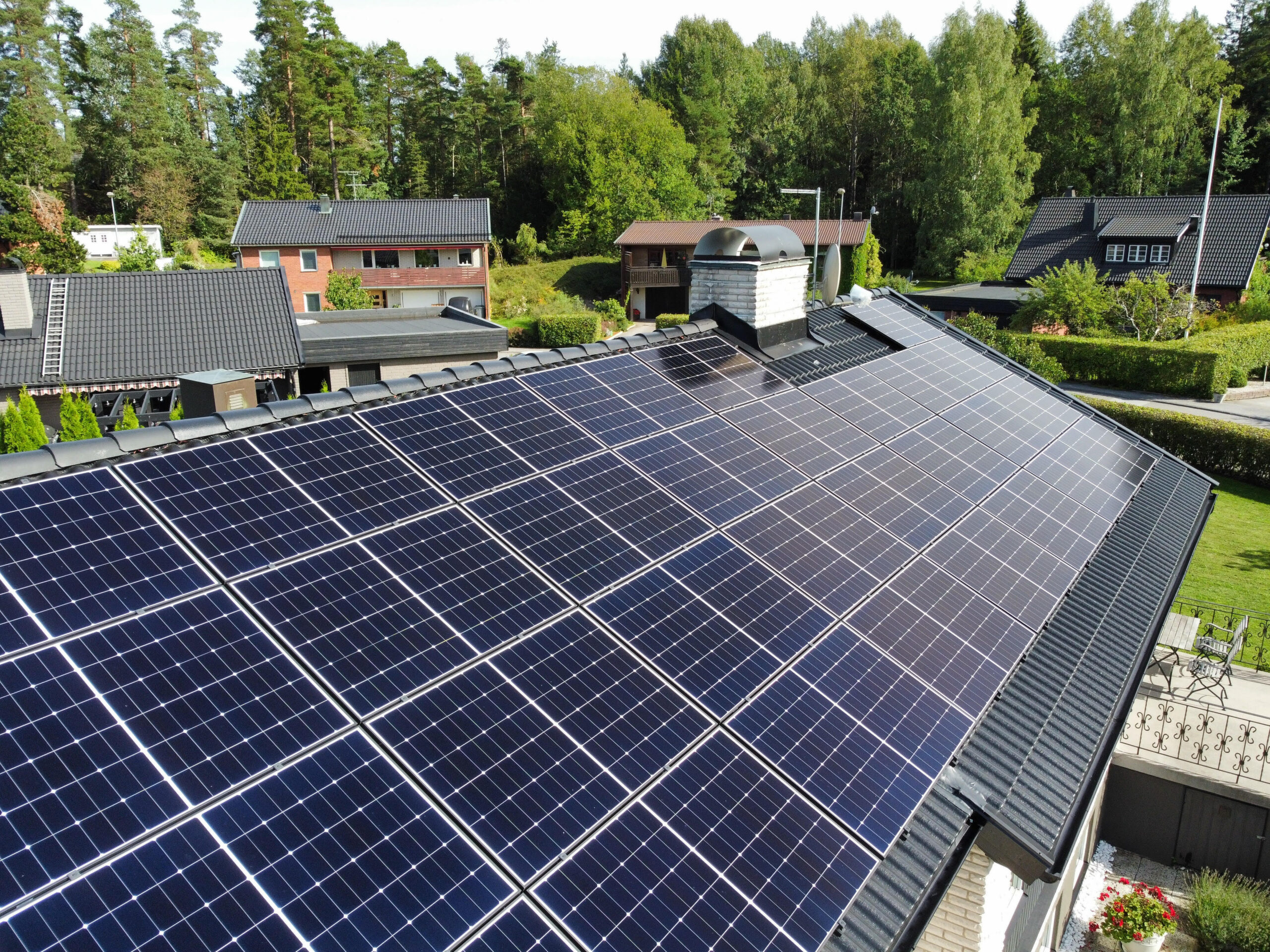 Närbild på ett hustak med solceller. Taket är gjort av svarta betongpannor. På taket finns en skorsten i tegel.