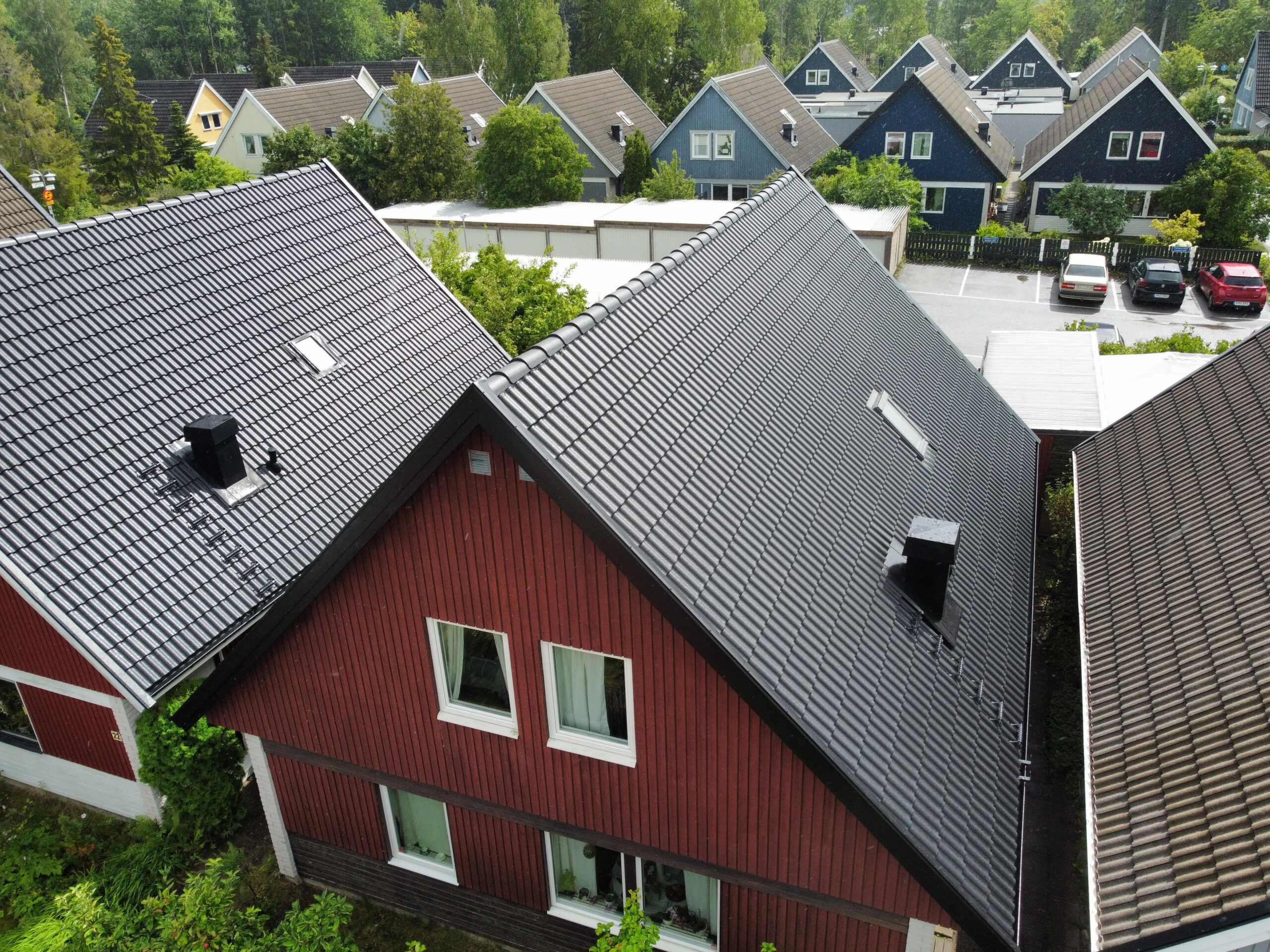 Ett rött hus med tak av sluttande betongpannor. I bakgrunden syns likande hus i andra färger.