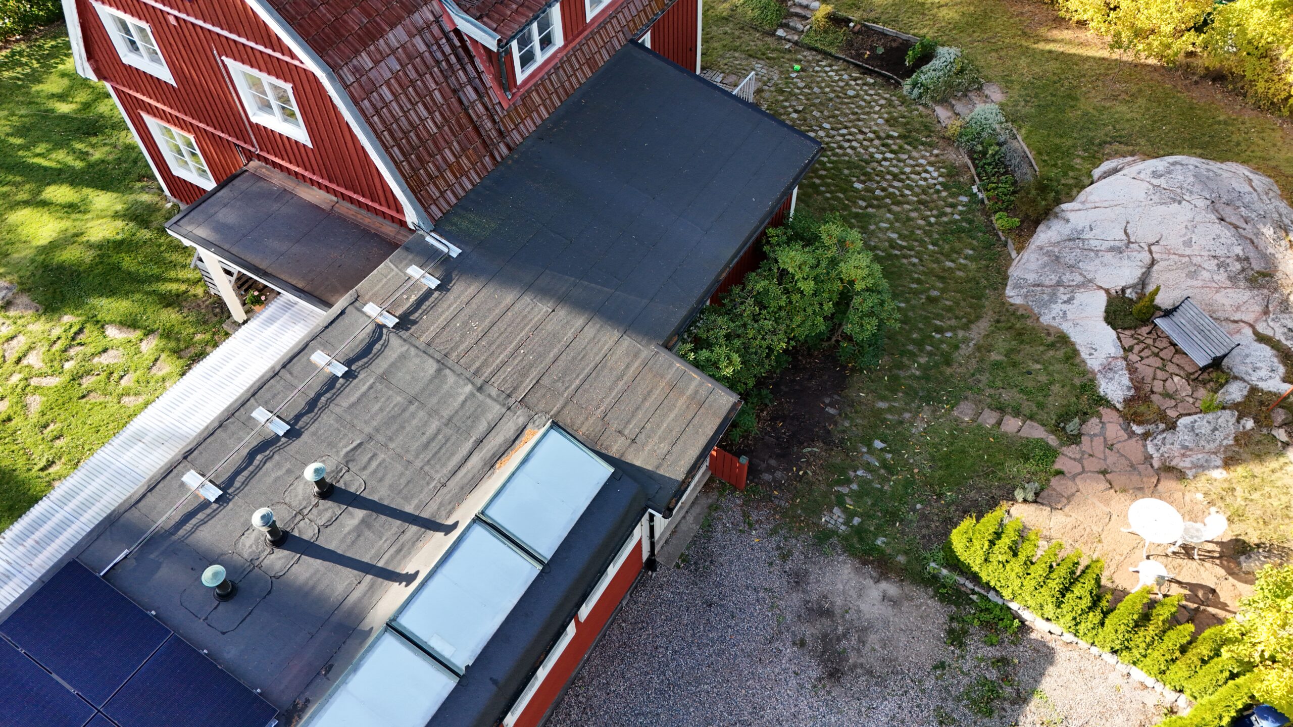 Fågelvy ovanför ett garagetak efter takomläggning med takpapp. På papptaket finns en skorsten i tegel och fem fönster.