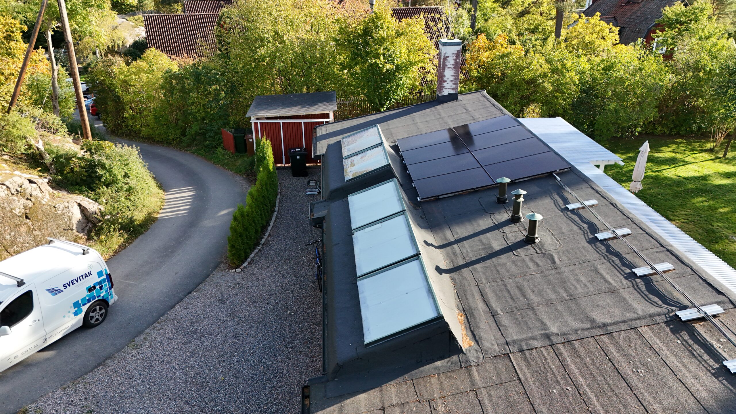 Fågelvy ovanför ett garagetak efter takomläggning med takpapp. På papptaket finns en skorsten i tegel, fem fönster och en panel med solceller.