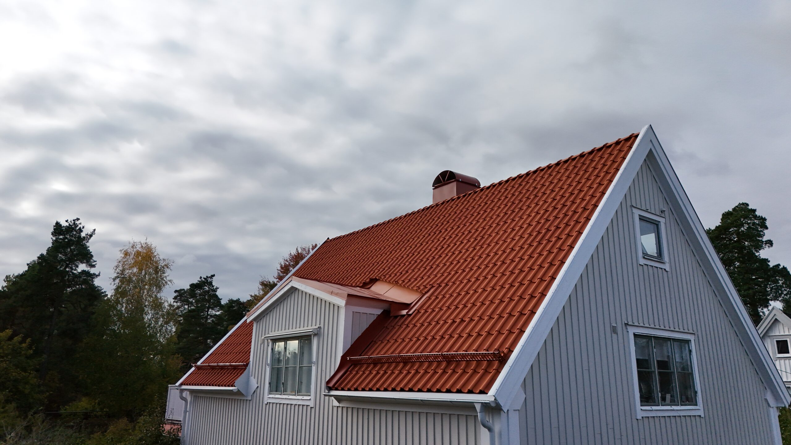 En grå villa med nylagt tak av tegelpannor, en skorsten i plåt samt snörasskydd.