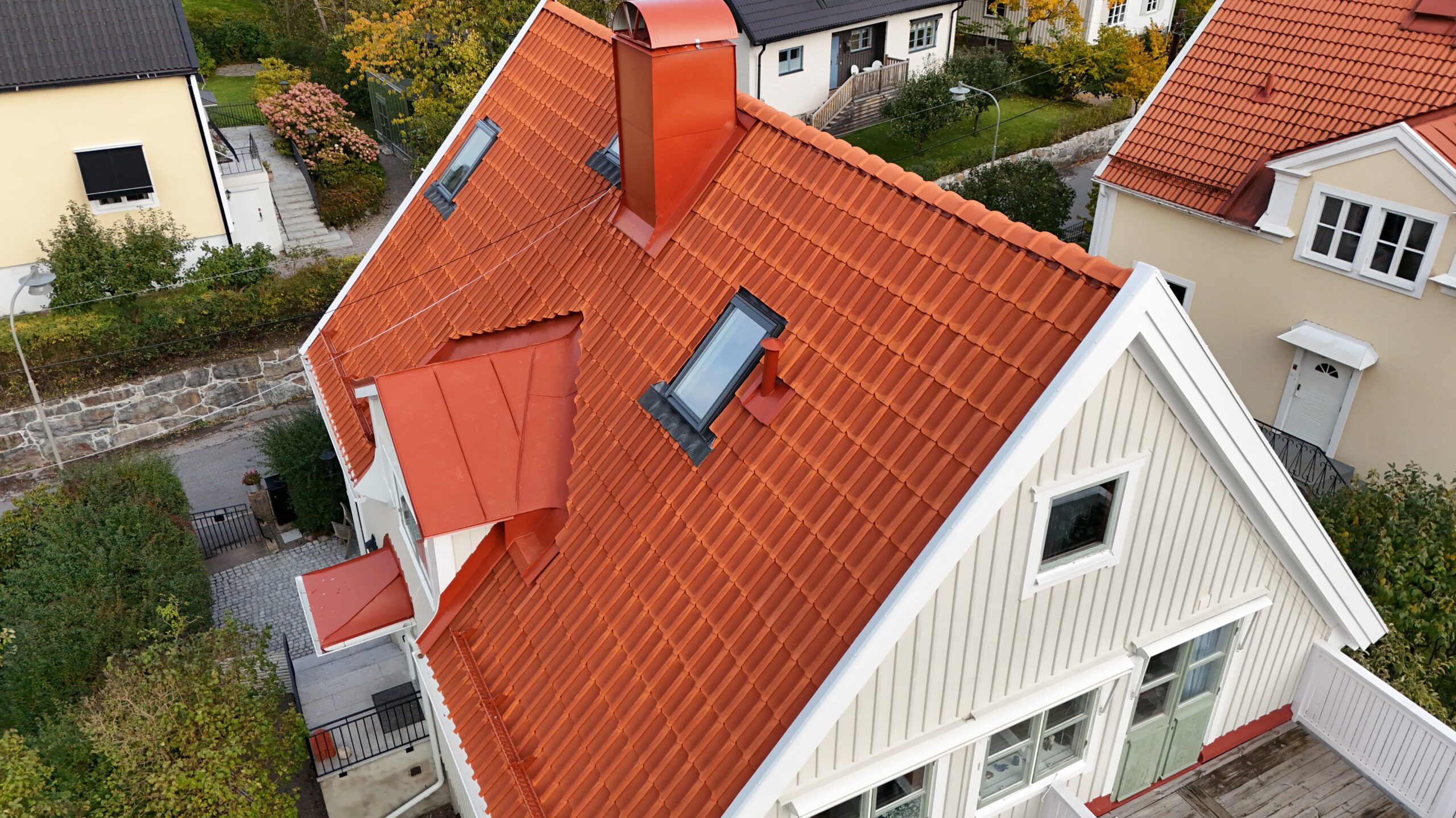 Fågelvy över en ville efter takomläggning. Taket är av tegelpannor, har detaljer plåt, tre fönster samt snörasskydd. I bakgrunden syns närliggande grannhus.