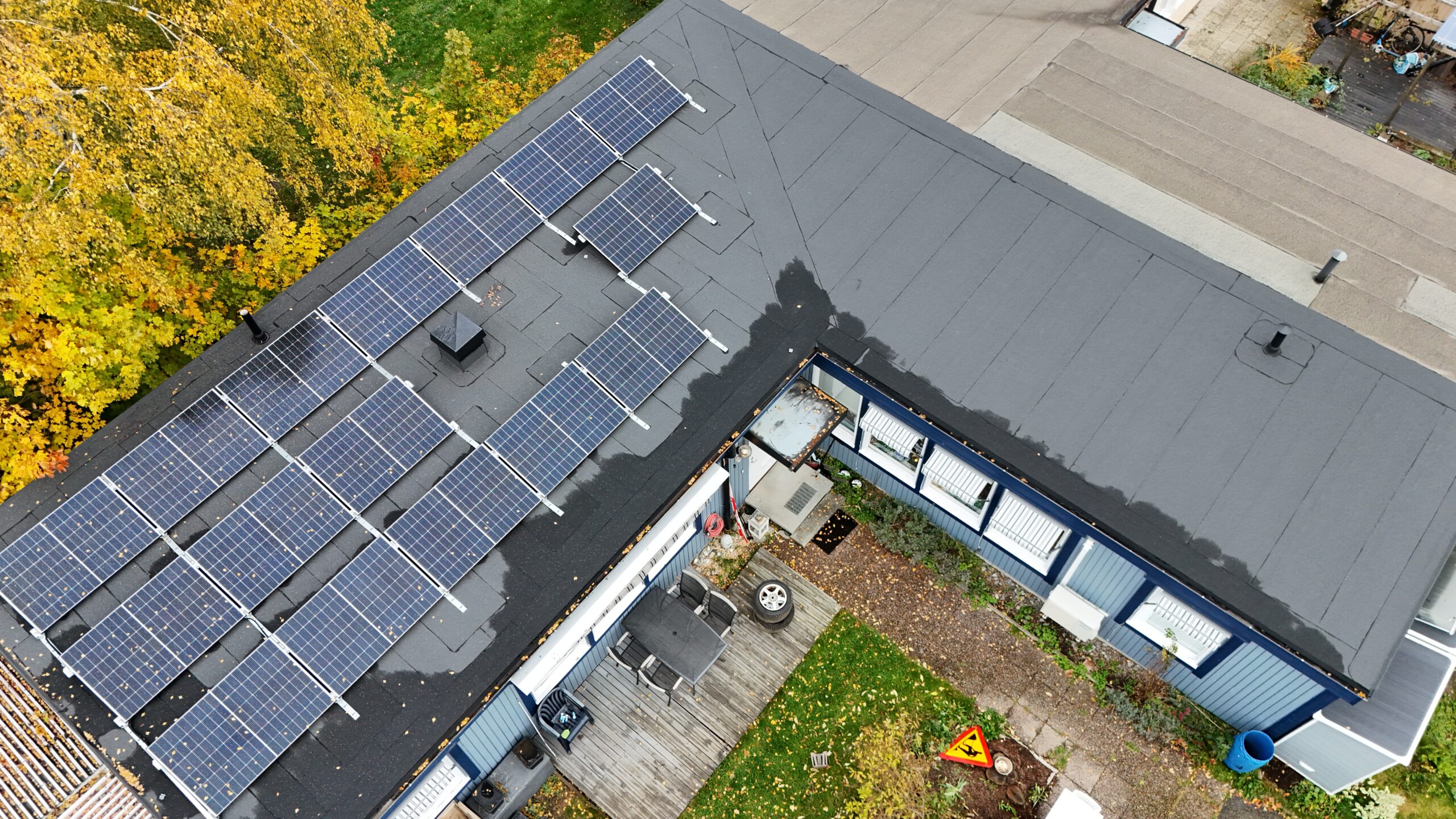 Fågelvy ovanför ett radhus med solceller och papptak. I bakgrunden syns tomten samt några träd.