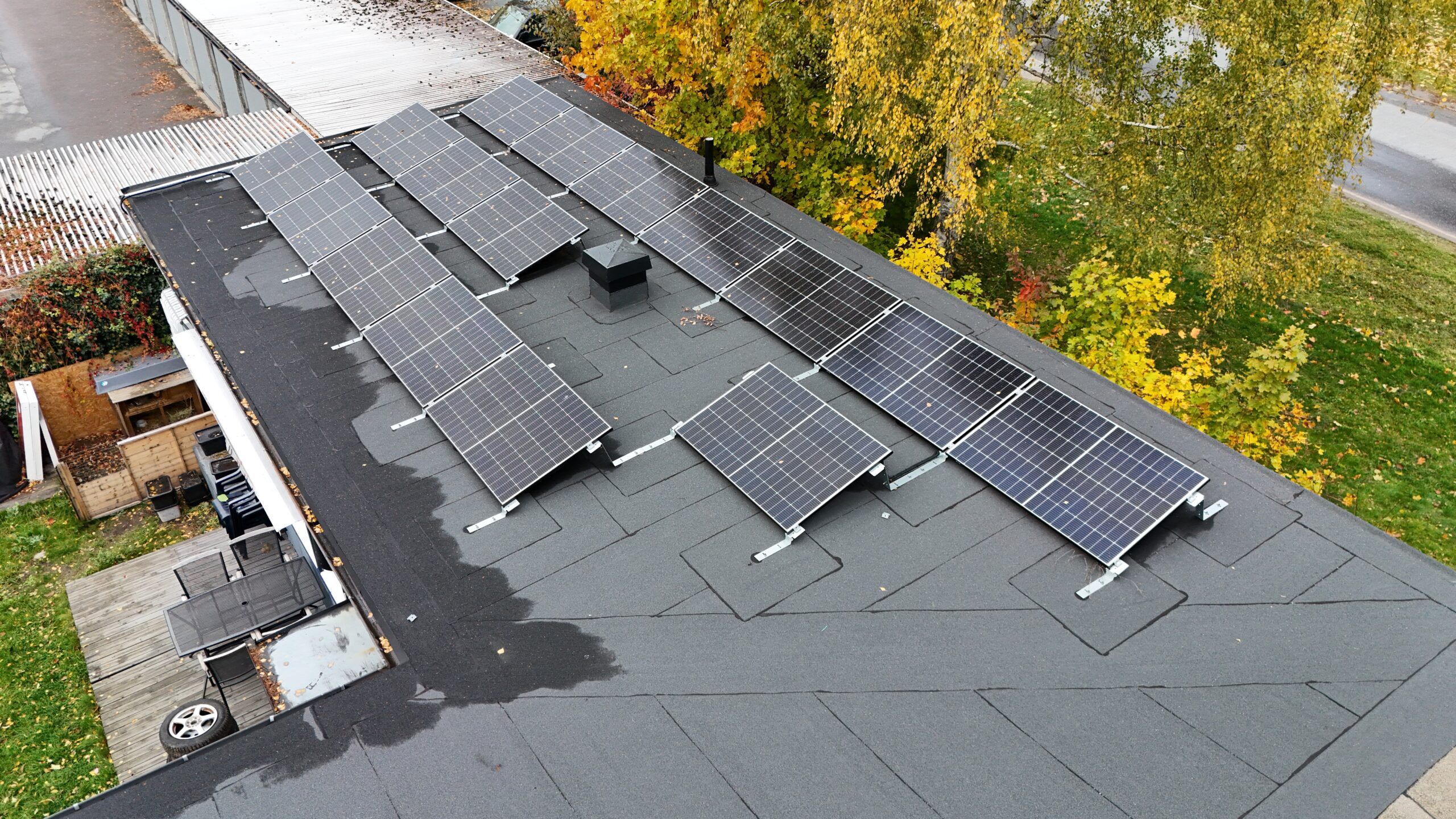 Fågelvy ovanför ett radhus med solceller och papptak. I bakgrunden syns tomten samt några träd.