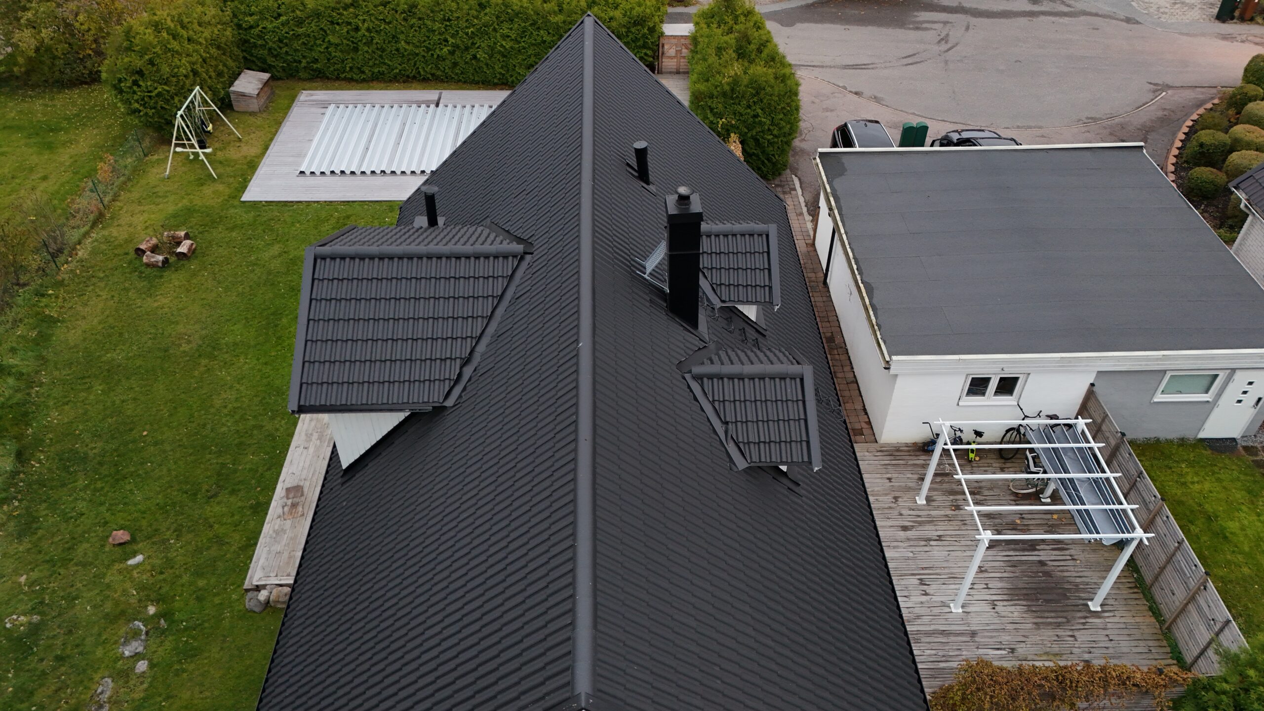 Fågelvy över ett hus med sluttande tak efter takomläggning. Taket är gjort av betongpannor, har tre utbuktningar för fönster och en skorsten. I bakgrunden syns tillhörande garage och husets tomt.