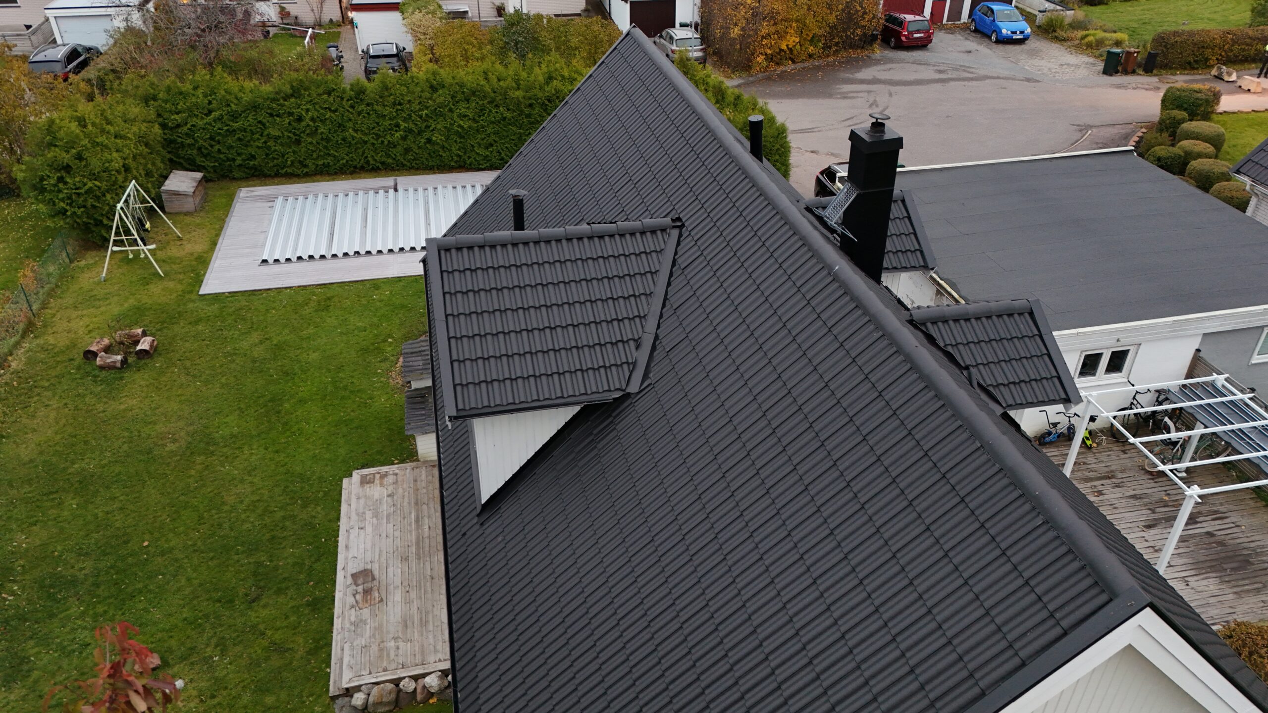 Fågelvy över ett hus med sluttande tak efter takomläggning. Taket är gjort av betongpannor, och har en utbuktning för fönster. I bakgrunden syns hustomten.