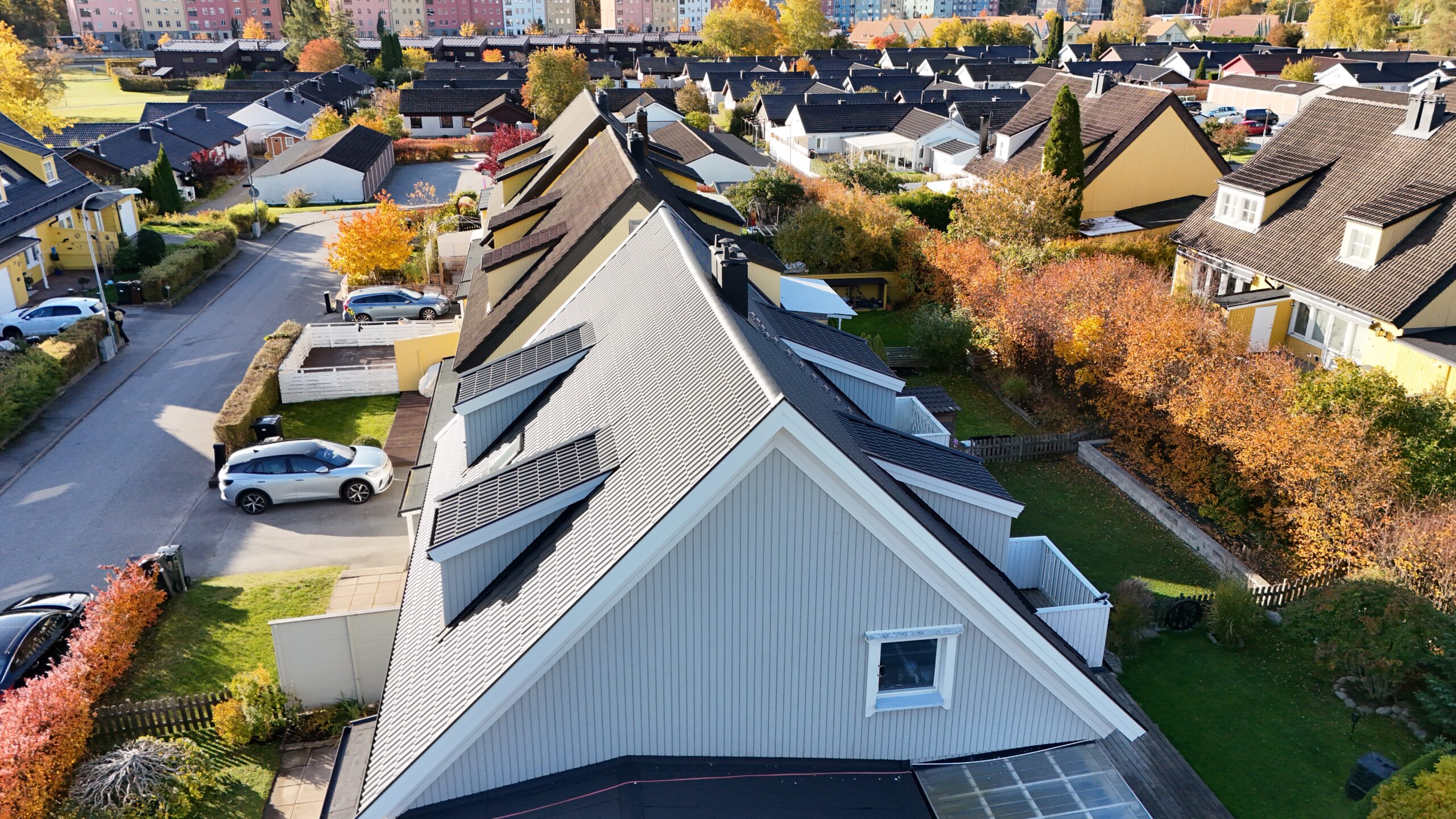 Fågelvy över hustak efter takomläggning med svarta betongpannor. På husgaveln sitter ett fönster. I bakgrunden syns närliggande grannhus.