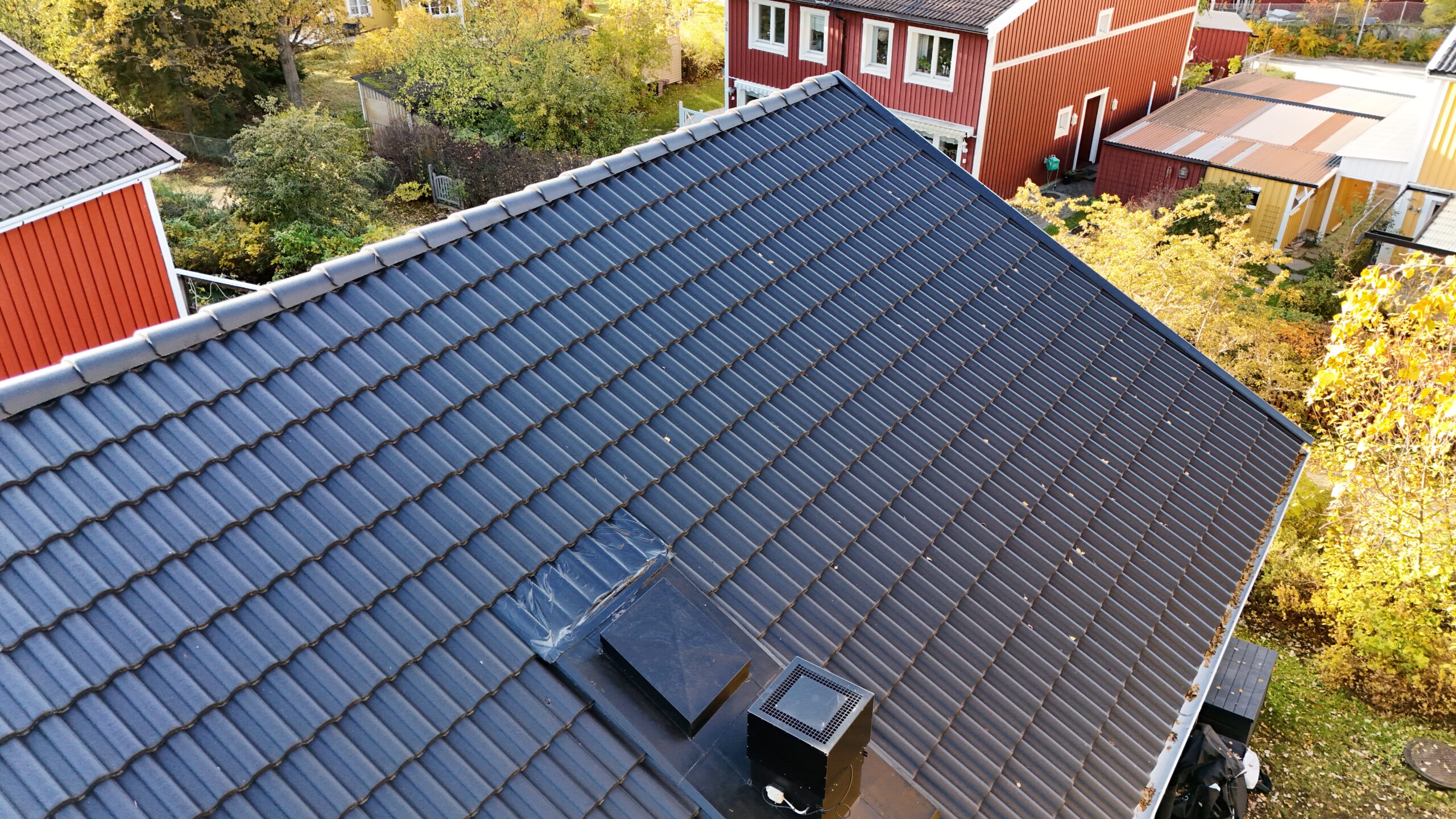 Närbild på hustak efter takomläggning med svarta betongpannor. I bakgrunden syns närliggande grannhus.