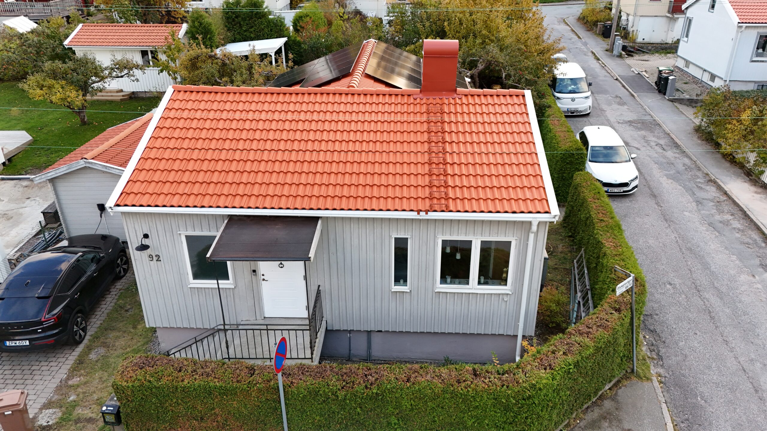 Fågelvy över hus och tak efter takomläggning. Hustaket är av tegelpannor, och har solceller, en takstege samt en skorsten i plåt. Runt huset syns delar av hustomten, samt tre parkerade bilar.