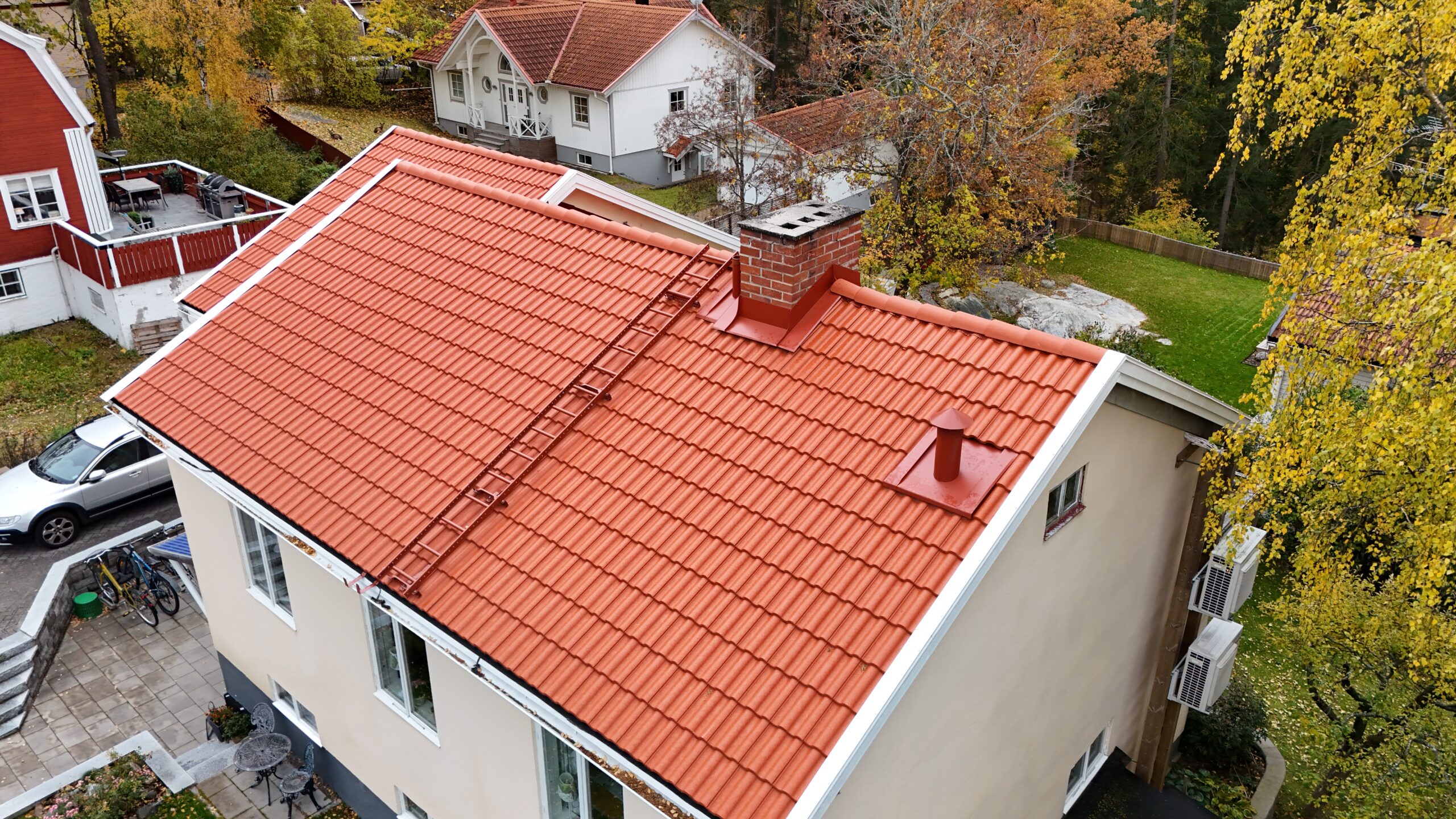 Fågelvy över hustak efter takomläggning. Taket är gjort av tegelpannor, har en skorsten och en takstege.