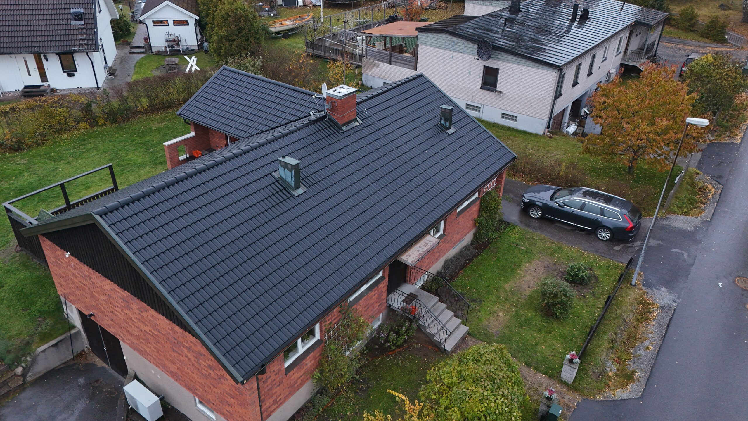 Fågelvy över ett omlagt tak på ett tegelhus. Hustaket är gjort med svarta betongpannor, och har en skorsten i tegel.