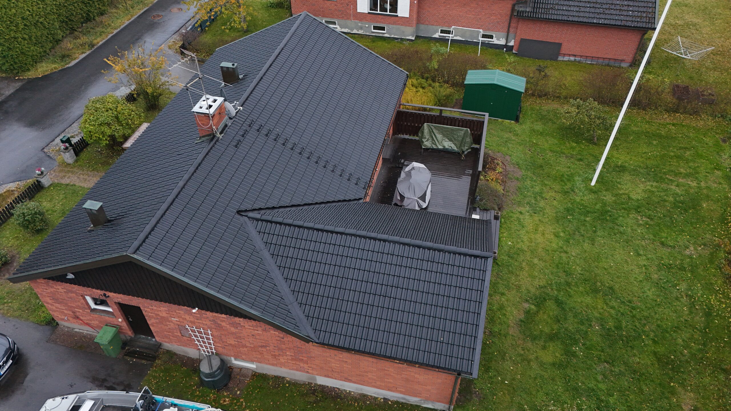 Fågelvy över ett omlagt tak på ett tegelhus. Hustaket är gjort med svarta betongpannor, har en skorsten i tegel samt en takstege på ena långsidan.