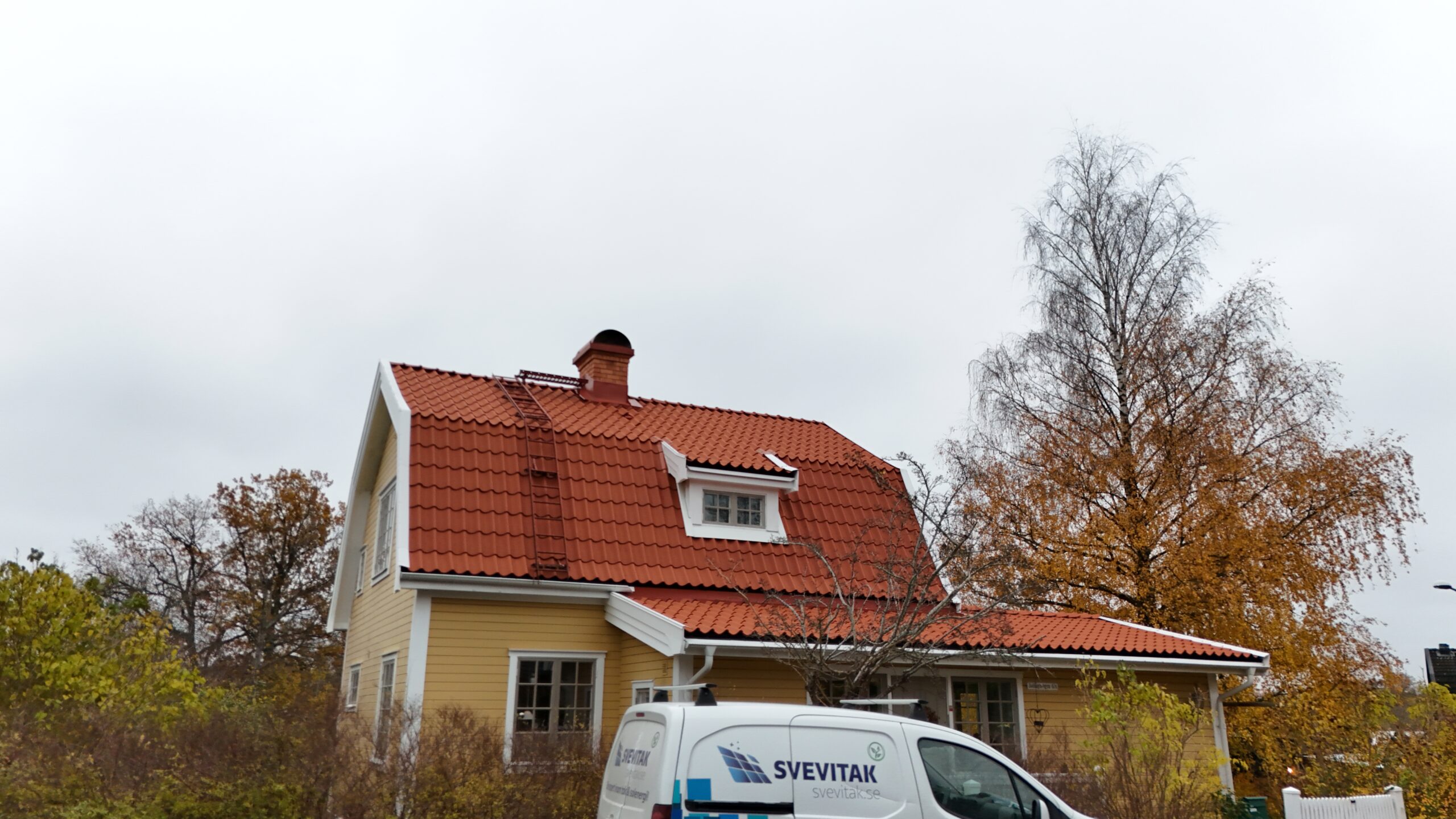 Gatuvy över en gul villa, med nylagt tegeltak. På taket finns en skorsten i tegel, snörasskydd samt en takstege.