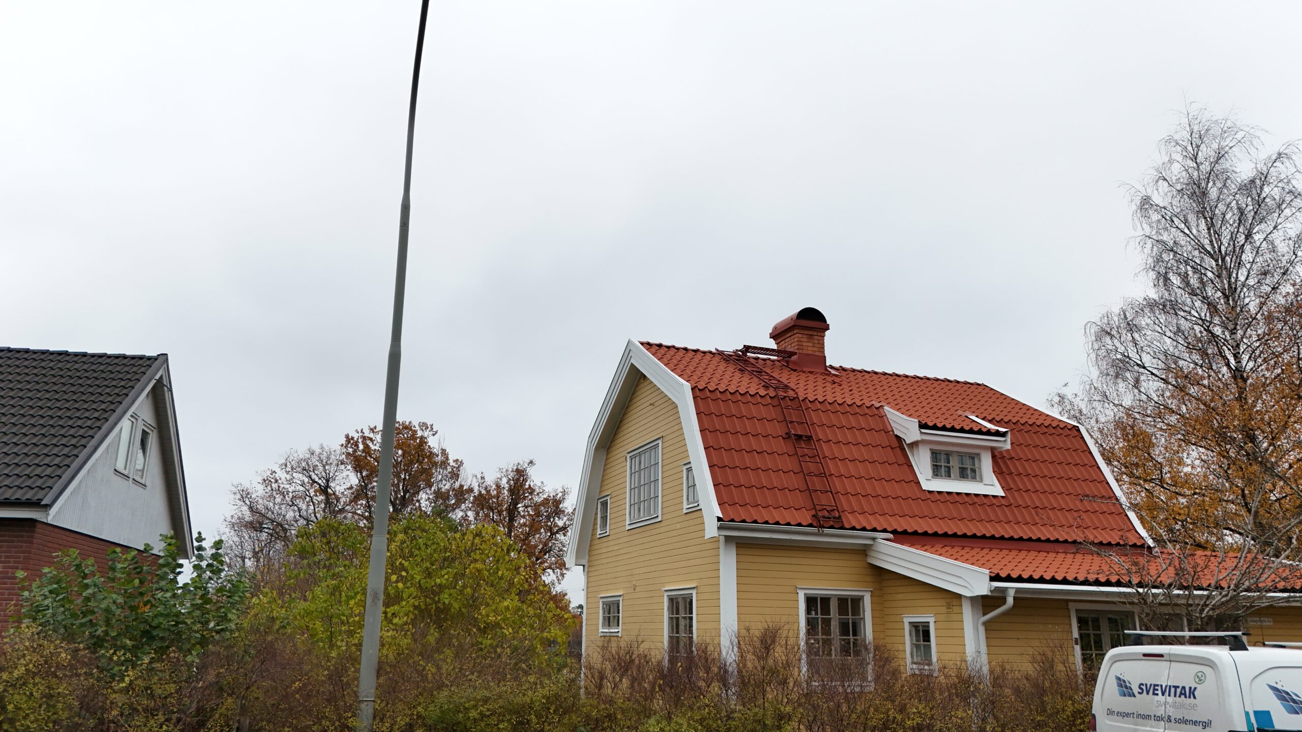 Gatuvy över en gul villa, med nylagt tegeltak. På taket finns en skorsten i tegel, snörasskydd samt en takstege.