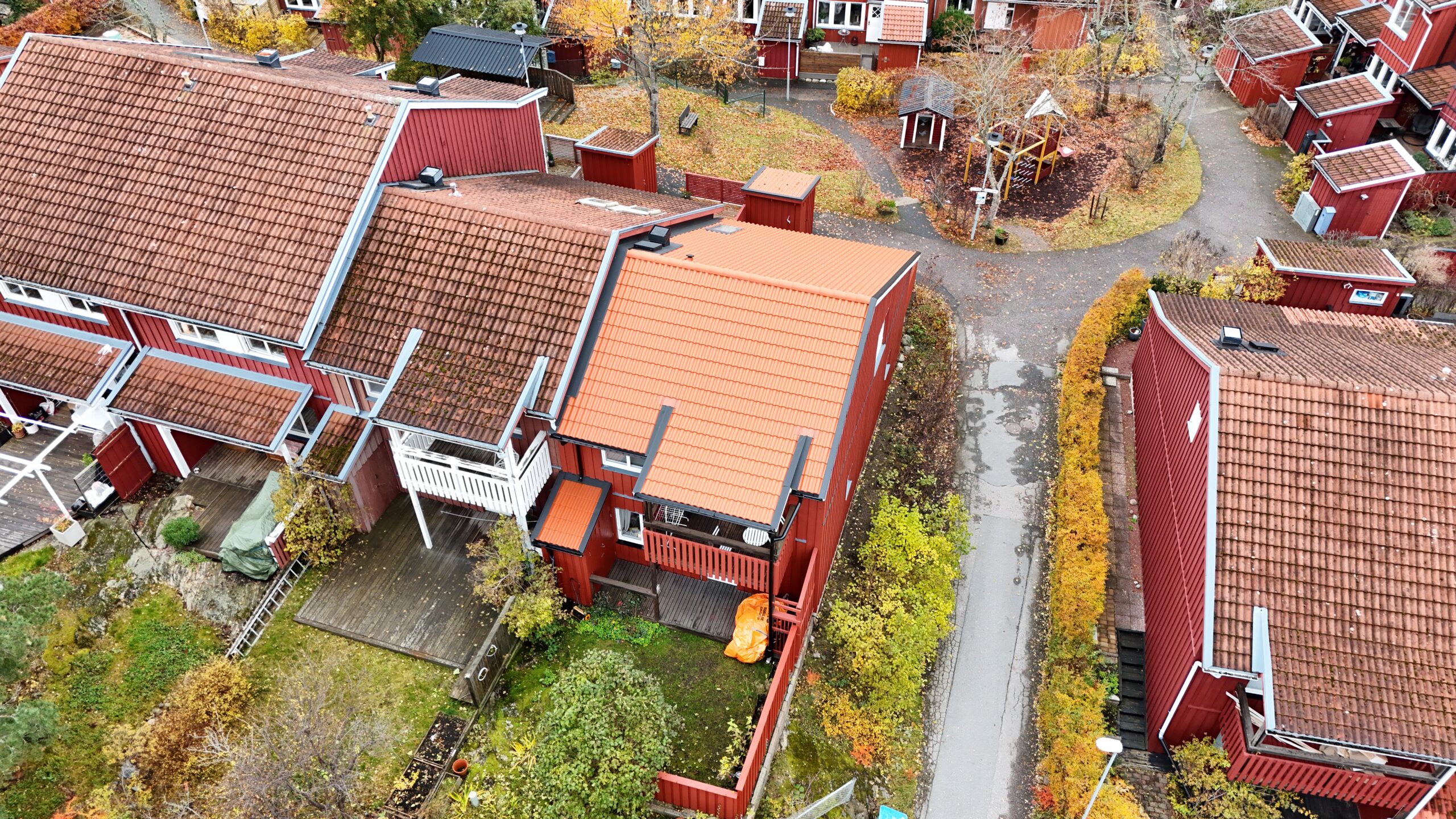 Fågelvy över rött radhus och närliggande grannhus. Taket är sluttande med nylagda tegelpannor.