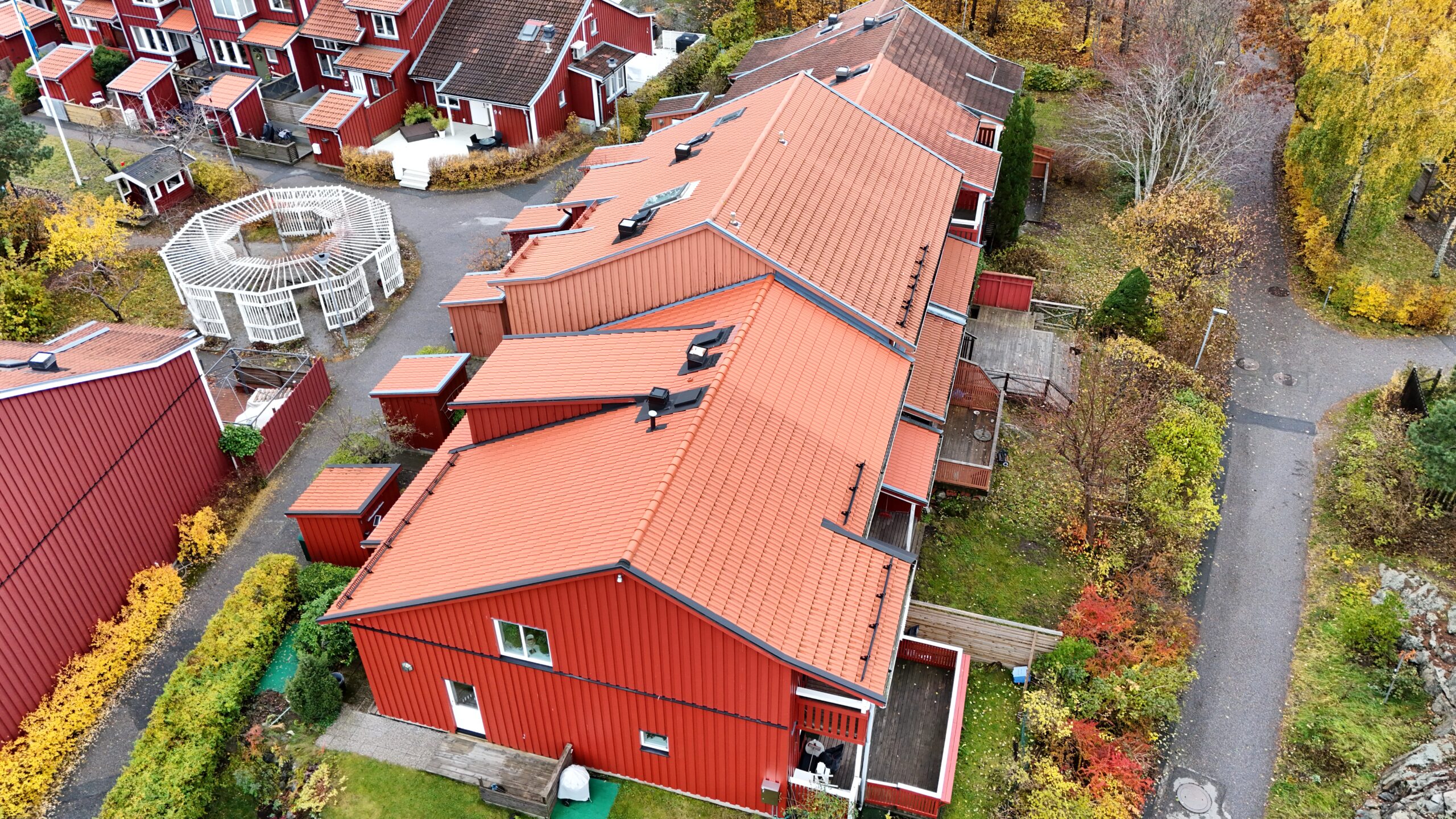 Fågelvy över radhuslänga som genomgått takomläggning. Taket är lätt sluttande och gjort med tegelpannor. På taken finns små fönster, skorstenar och snörasskydd.