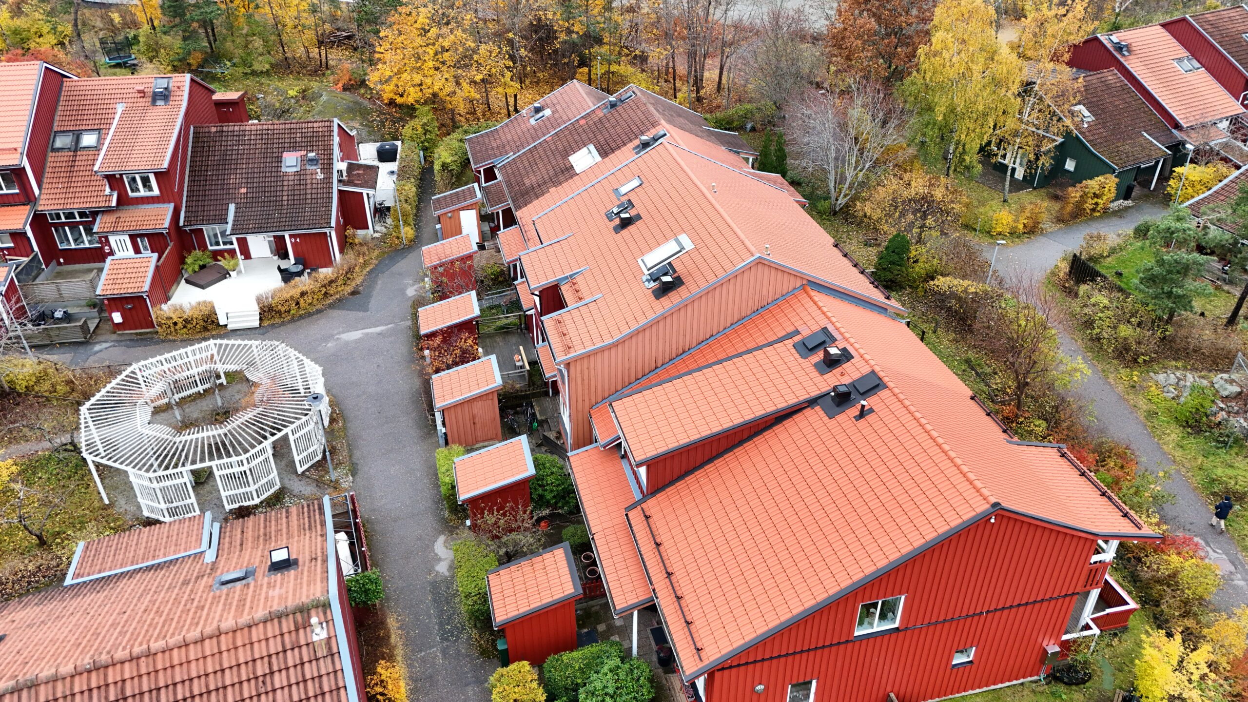 Fågelvy över radhuslänga som genomgått takomläggning. Taket är lätt sluttande och gjort med tegelpannor. På taken finns små fönster, skorstenar och snörasskydd.