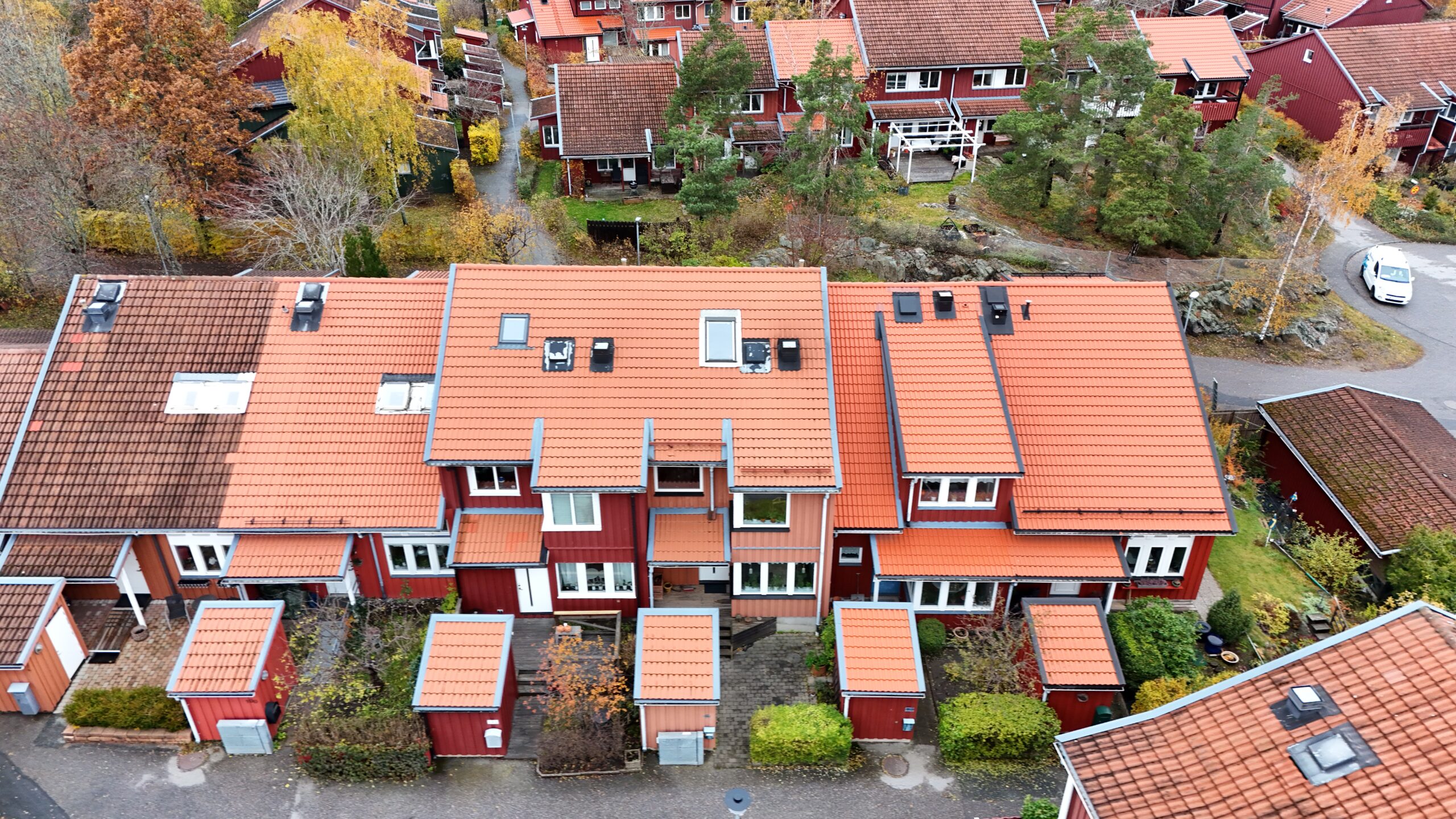 Fågelvy över radhuslänga som genomgått takomläggning. Taket är lätt sluttande och gjort med tegelpannor. På taken finns små fönster, skorstenar och snörasskydd.