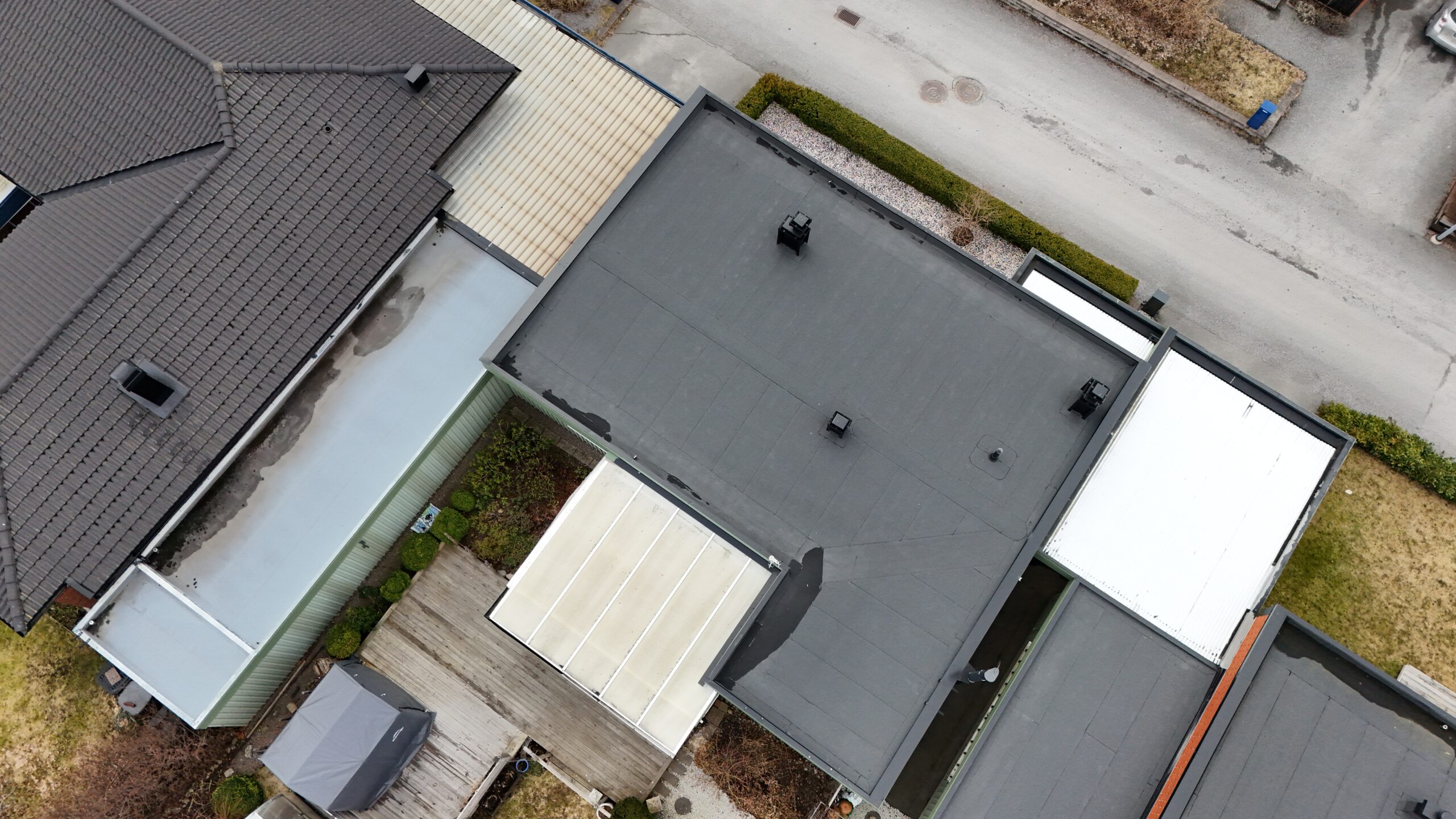 Fågelvy över kedjehus efter takomläggning med asfaltpapp. Runt huset ligger grannhus.