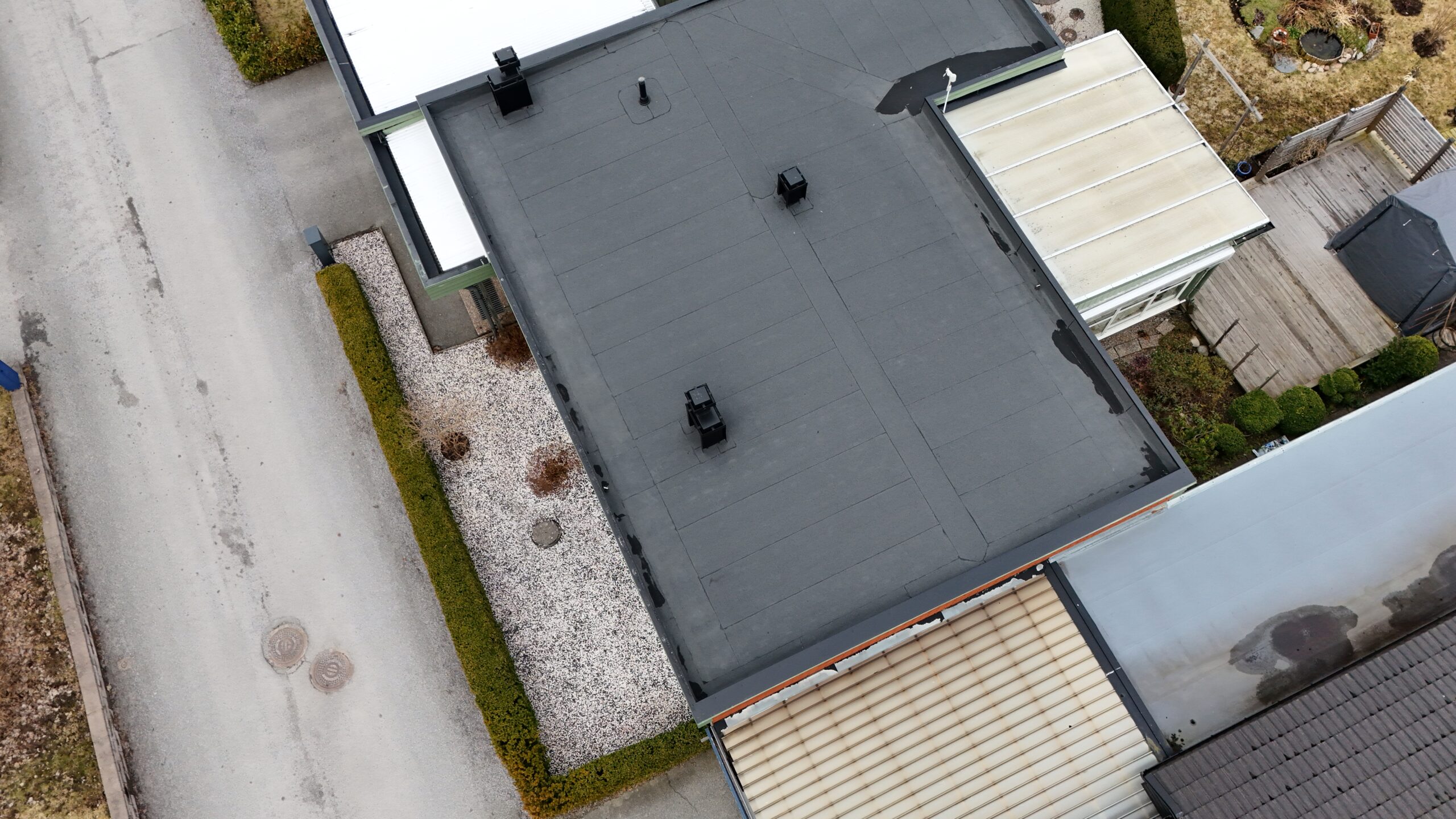 Fågelvy över kedjehus efter takomläggning med asfaltpapp. Runt huset ligger grannhus.