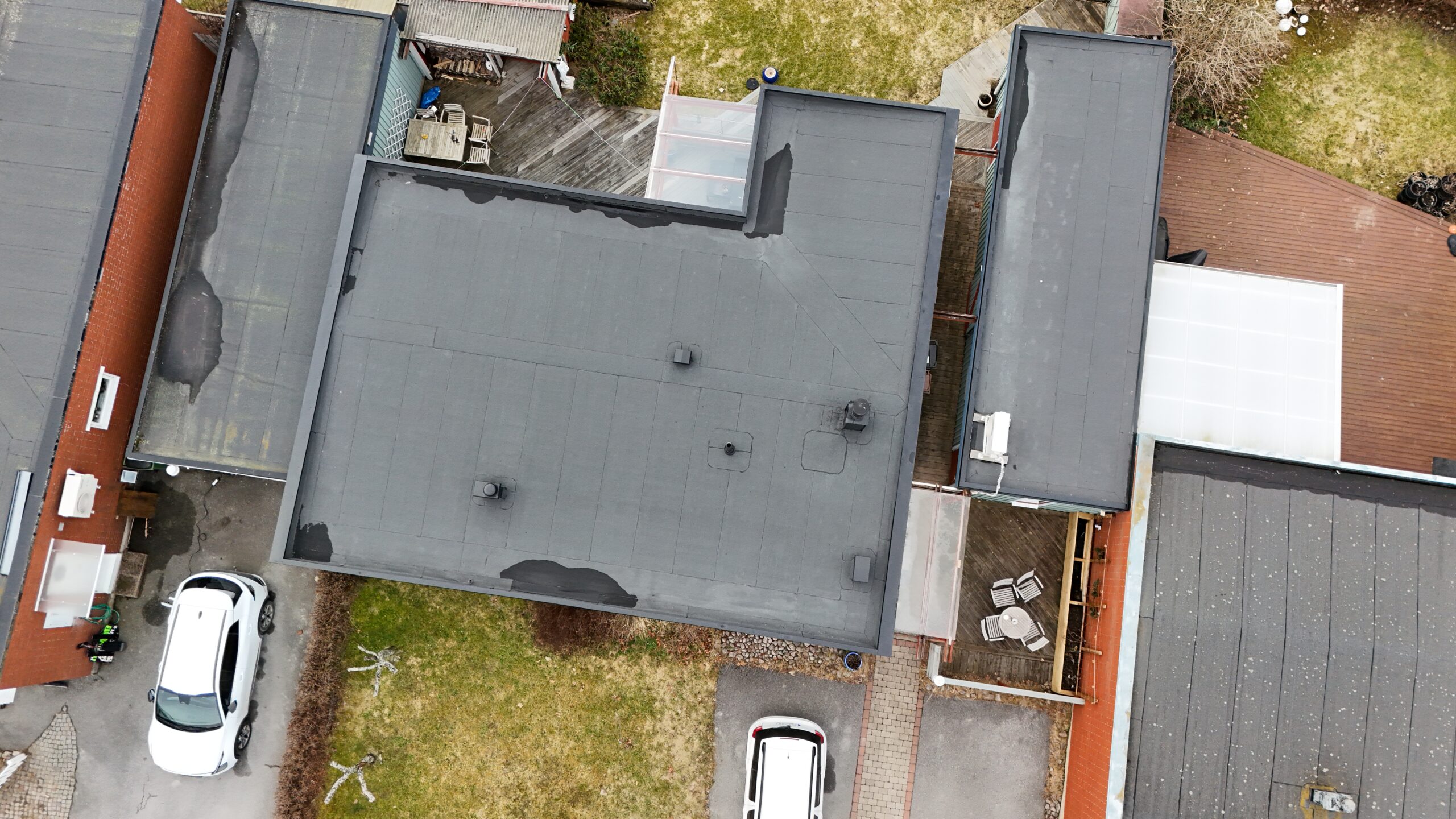 Fågelvy över kedjehus efter takomläggning med asfaltpapp. Runt huset ligger grannhus och 2 parkerade bilar står på uppfarten.