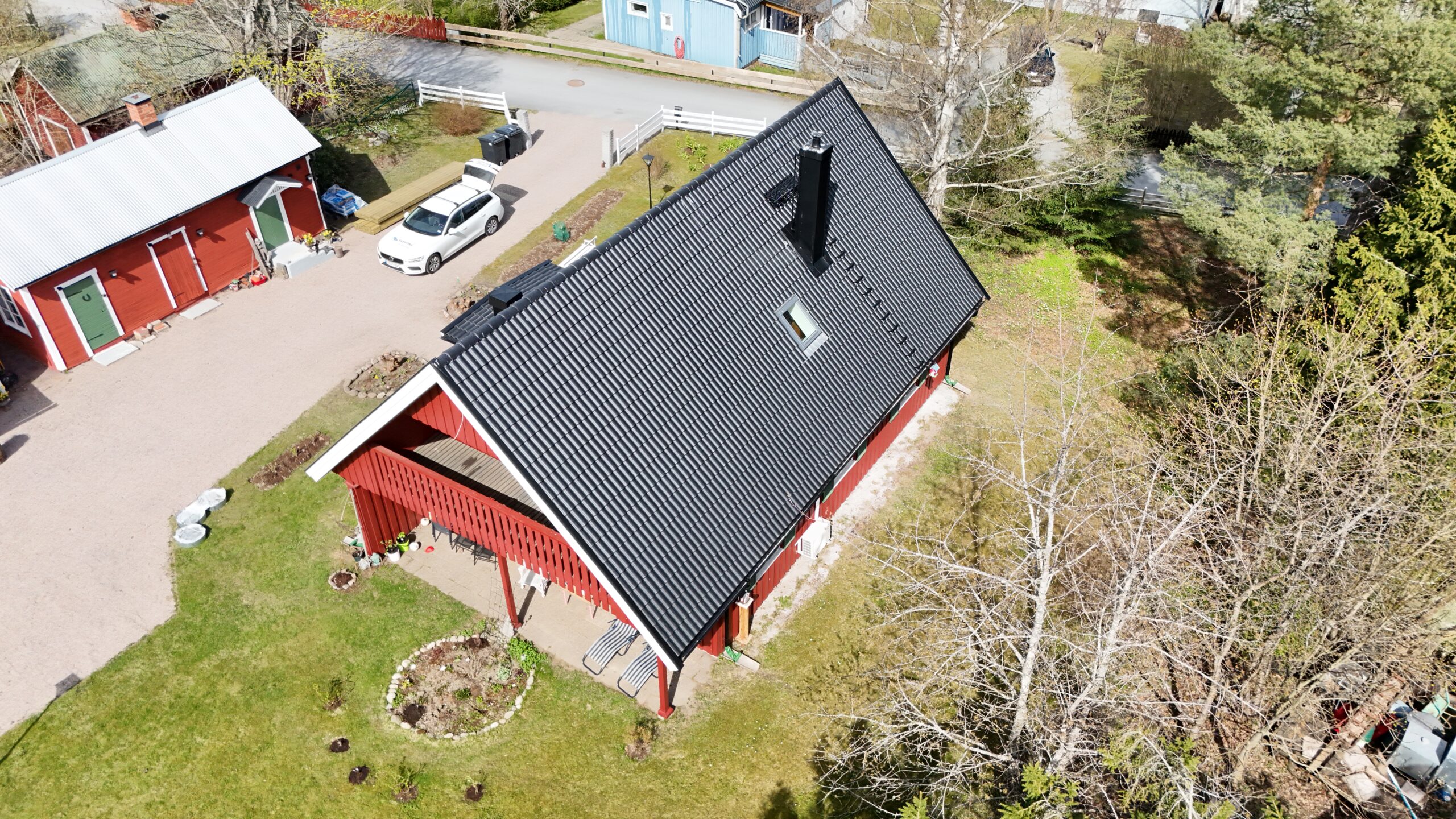 Fågelvy över ett omlagt hustak med betongpannor. Huset är rött och står på en stor tomt med gräsmatta och träd.