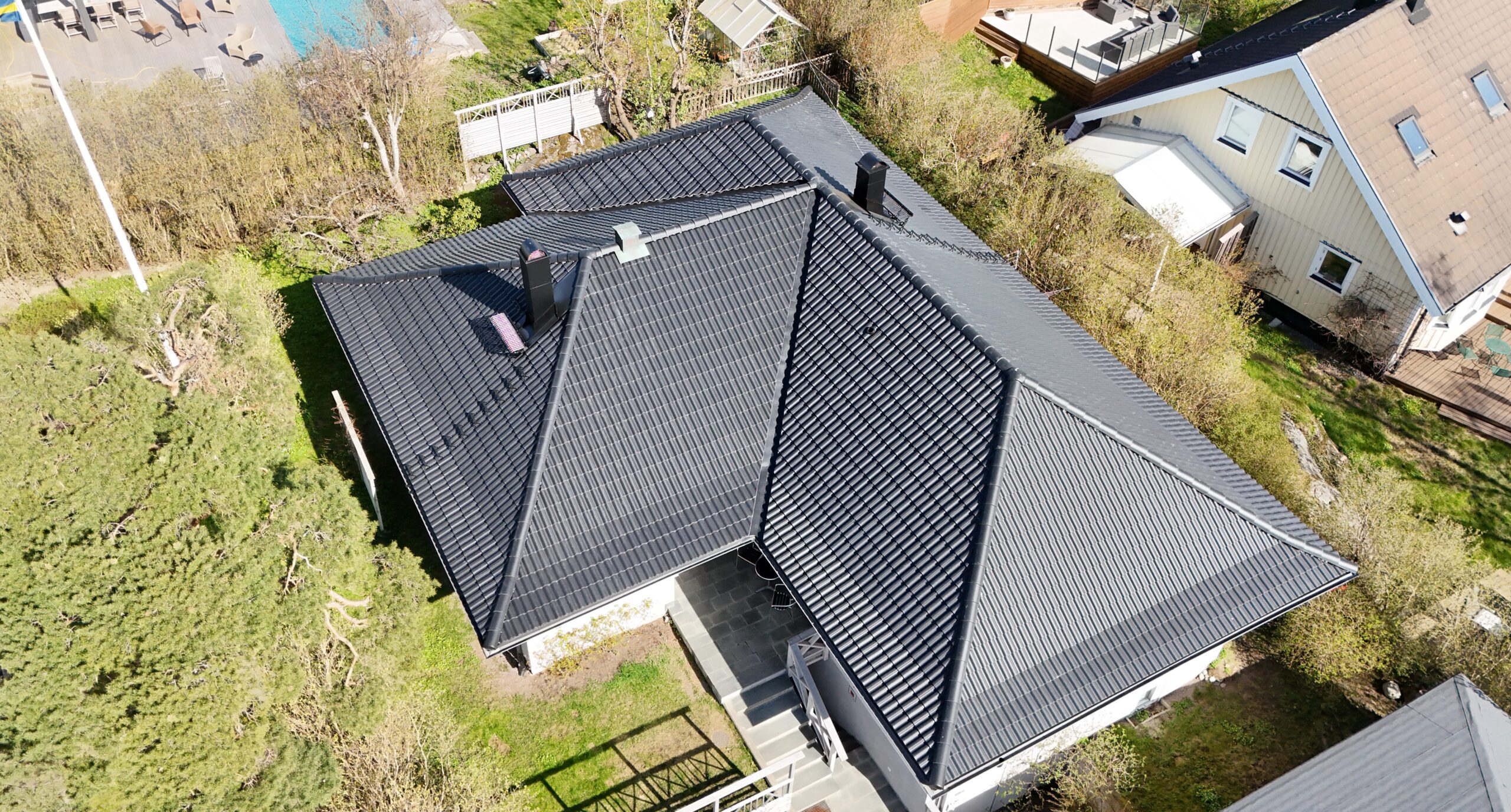 Fågelvy över ett hus med omlagt tak med svarta betongpannor. Runt huset växer det buskar och träd.