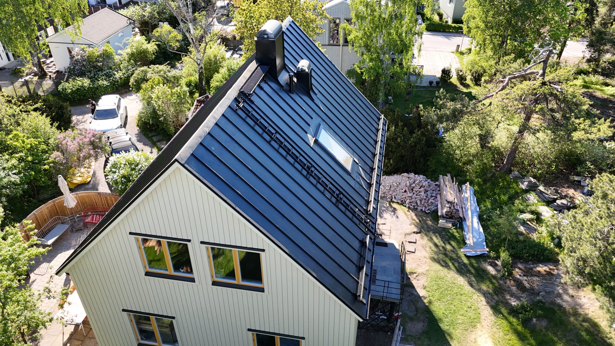 Fågelvy på husgavel och sluttande tak. Hustaket är gjort av bandtäckt plåt och har en skorsten, takstege och snörasskydd.