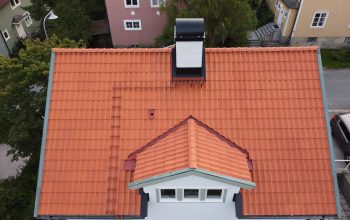 Fågelvy över ett vitt hus med sluttande tak av tegelpannor.