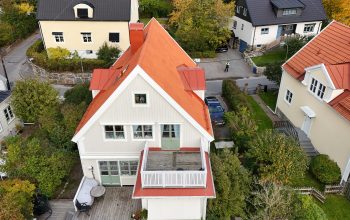 Fågelvy över ett villahus efter takomläggning. Taket är kombinerat med tegelpannor och bandtäckt plåt. I bakgrunden syns närliggande grannhus.