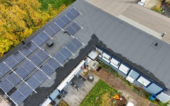 Fågelvy ovanför ett radhus med solceller och papptak. I bakgrunden syns tomten samt några träd.