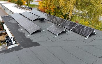 Närbild ovanpå ett radhus med solceller på papptaket. I bakgrunden syns områdets garage samt några träd.