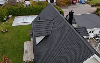 Fågelvy över ett hus med sluttande tak efter takomläggning. Taket är gjort av betongpannor, och har en utbuktning för fönster. I bakgrunden syns hustomten.