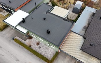 Fågelvy över ett grönt kedjehus efter takomläggning med asfaltpapp. Runt huset ligger grannhus.