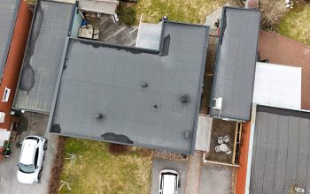 Fågelvy över kedjehus efter takomläggning med asfaltpapp. Runt huset ligger grannhus och 2 parkerade bilar står på uppfarten.