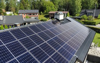 Närbild på ett hustak med solceller. Taket är gjort av svarta betongpannor. På taget finns en skorsten i tegel.